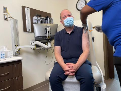 Governor Polis wearing a mask and receiving a vaccination.